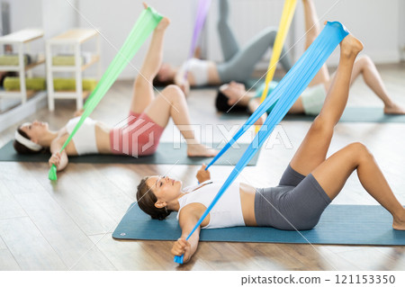 Girl lying and perform variety of exercises to strengthen muscles of press with wide resistance band 121153350