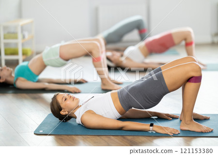 Girls perform exercises lying on side with legs straightened and narrow elastic band on shins 121153380