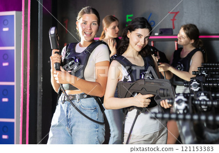 Portrait of two positive girls in special vests playing laser tag with friends on bachelorette Portrait of two positive girls in special vests playing laser tag with friends on bachelorette 121153383
