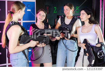 Group of girls in laser tag vests with rifles in their hands are discussing the rules of game of laser tag Group of girls in laser tag vests with rifles in their hands are discussing the rules of game of laser tag 121153397