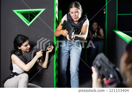 Team of young girlfriends play laser tag in labyrinth. Girls spend time actively Team of young girlfriends play laser tag in labyrinth. Girls spend time actively 121153404
