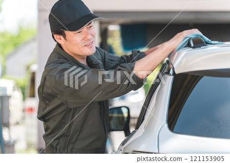 A male mechanic wearing overalls washing a car 121153905