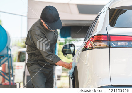 A male mechanic wearing overalls washing a car A male mechanic wearing overalls washing a car 121153906
