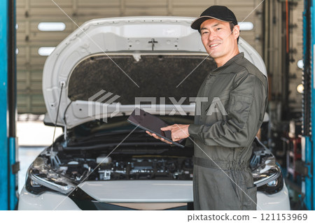 男性汽車機械師使用平板電腦檢查汽車的引擎室 男性汽車機械師使用平板電腦檢查汽車的引擎室 121153969