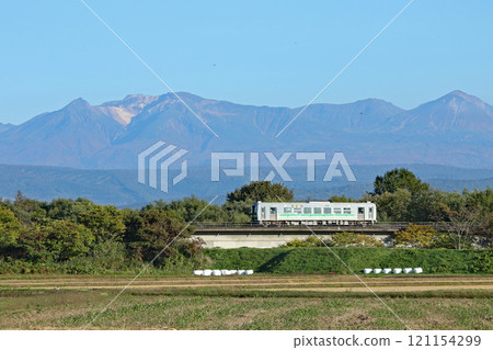 A local train on the Soya Main Line running with Mount Daisetsu in the background - JR Hokkaido H100 DECMO 121154299