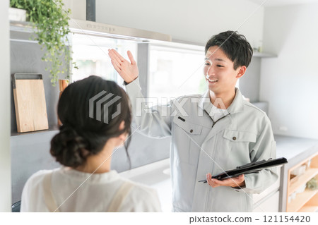 A woman, a housewife, receives an explanation about ventilation fans and range hoods, and a man in work clothes from a construction company, equipment store, electrician, and contractor. 121154420