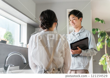 一名在水管工/設備店工作的男子向廚房裡的家庭主婦解釋水管工/設備。 一名在水管工/設備店工作的男子向廚房裡的家庭主婦解釋水管工/設備。 121154529