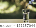 Water from plastic bottle pouring into glass on table with nature background 121157044