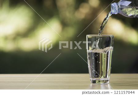 Water from plastic bottle pouring into glass on table with nature background Water from plastic bottle pouring into glass on table with nature background 121157044