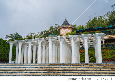 Many stone columns in the ancient style rise in a luxurious garden full of greenery. 121157791