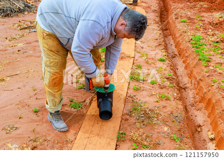 Man is fixing drainage pipe for enhance water flow management in freshly dug earth trench Man is fixing drainage pipe for enhance water flow management in freshly dug earth trench 121157950