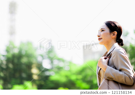 A woman in a suit walking outdoors among the fresh greenery and looking up 121158134