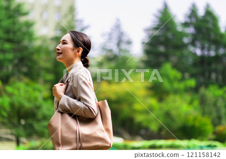 一位穿著西裝的女人在戶外新鮮的綠色植物中行走時抬起頭來 一位穿著西裝的女人在戶外新鮮的綠色植物中行走時抬起頭來 121158142