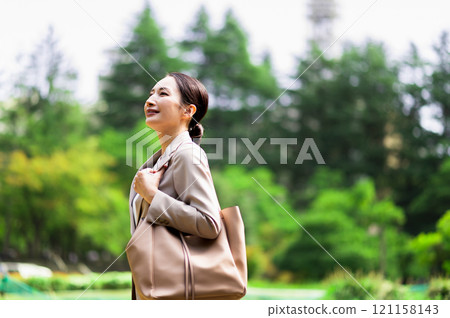 一位穿著西裝的女人在戶外新鮮的綠色植物中行走時抬起頭來 121158143