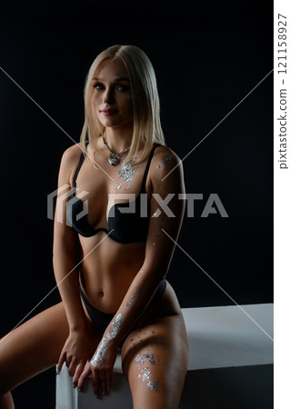 Model posing in black lingerie with decorative body art in a dark studio 121158927