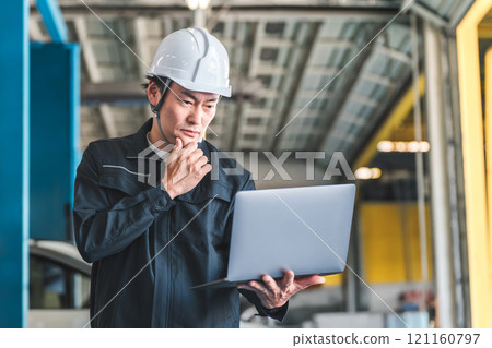 在工廠、倉庫或配送中心，男性工人一邊看電腦一邊開會（思考、遇到麻煩、擔心、研究） 121160797