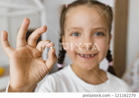 Excited young Caucasian girl displaying fallen baby tooth, symbolizing childhood milestones. Smiling child delighted by tooth loss experience, emphasizing home environment and growth. 121162270
