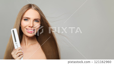 Excited smiling woman with long straight healthy hairstyle using straightening iron Excited smiling woman with long straight healthy hairstyle using straightening iron 121162960