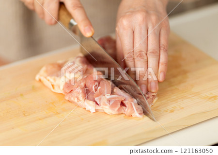 Hands of a middle-aged to senior woman cutting chicken in the kitchen Hands of a middle-aged to senior woman cutting chicken in the kitchen 121163050