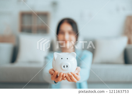 Young Asian woman holding piggy bank and sitting on the floor at home 121163753