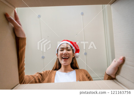 Low angle view of surprised young Asian woman wearing Christmas hat and unpacking 121163756