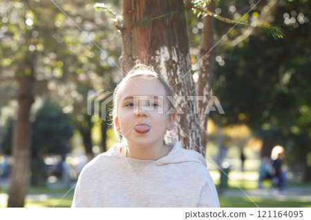 Funny child smiling and sticking out tongue, outdoors portrait. Happiness and childhood concept Funny child smiling and sticking out tongue, outdoors portrait. Happiness and childhood concept 121164095
