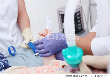Child is under general anesthesia. Child's hand in close-up. Pulse oximeter is located on child's fingers. Device for measuring oxygen levels and heart rate. Breathing apparatus. Child is under general anesthesia. Child's hand in close-up. Pulse oximeter is located on child's fingers. Device for measuring oxygen levels and heart rate. Breathing apparatus. 121164536