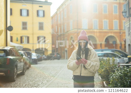 A Young Woman Engaged in Texting While Strolling Through a Bright and Colorful European Street A Young Woman Engaged in Texting While Strolling Through a Bright and Colorful European Street 121164622