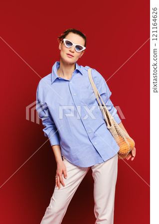 Chic woman poses with stylish sunglasses against a vibrant red background 121164626