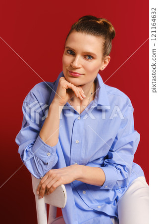 Woman in a blue shirt poses thoughtfully against a red backdrop Woman in a blue shirt poses thoughtfully against a red backdrop 121164632