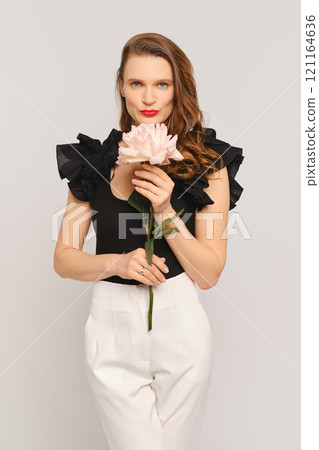 Model with flower poses elegantly in contemporary fashion studio setting Model with flower poses elegantly in contemporary fashion studio setting 121164636