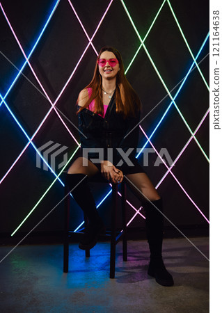 Young woman poses confidently in stylish outfit with neon light backdrop 121164638