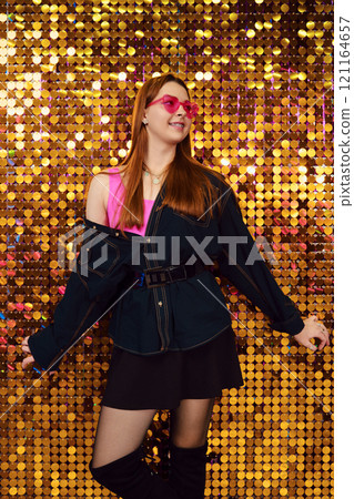 Young woman posing confidently in trendy outfit against a sparkling golden backdrop Young woman posing confidently in trendy outfit against a sparkling golden backdrop 121164657