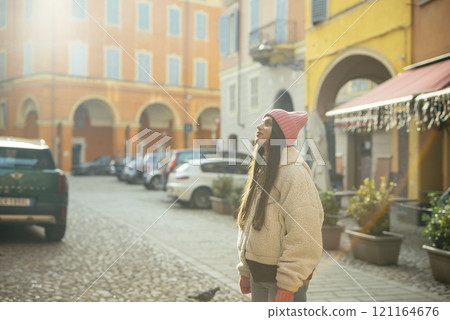 A woman in cozy clothing enjoys a warm, sunny day in a vibrant, colorful urban setting 121164676