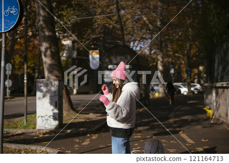 A woman enjoys a beautiful Autumn Park day while using her smartphone for activities 121164713