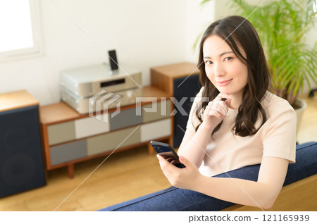 A woman sitting on a sofa in the living room looking at her smartphone 121165939