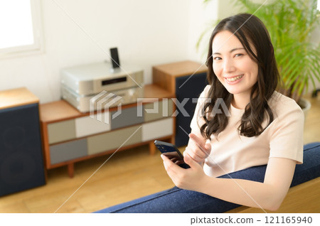 一位女士坐在客廳的沙發上,看著她的智慧型手機 一位女士坐在客廳的沙發上,看著她的智慧型手機 121165940