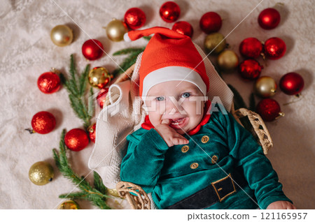 Merry Christmas and Happy New Year. A cheerful little child in a New Year's costume lies in a basket with Christmas tree balls 121165957