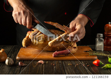 The chef expertly carves golden raw chicken surrounded by fresh herbs and vegetables, showcasing culinary skill and delicious aromas in the warm atmosphere of the restaurant kitchen 121166159