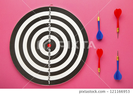 Dart board with red and blue darts on pink background. 121166953
