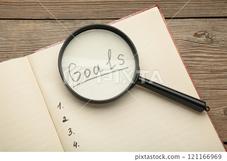 My Goals as memo on notebook with magnifying glass on grey wooden background. My Goals as memo on notebook with magnifying glass on grey wooden background. 121166969