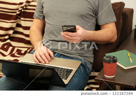 Young man working at home using laptop and smartphone Young man working at home using laptop and smartphone 121167284