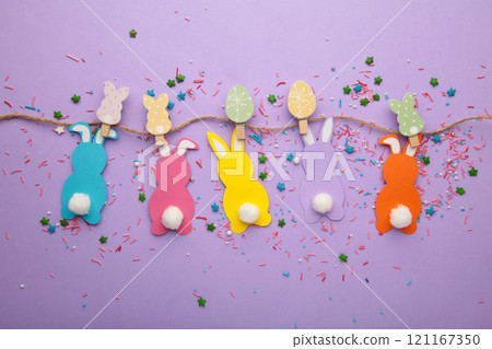 Easter rabbits handmade from colored paper on a rope with clothespins easy crafts for children on a purple background. Easter rabbits handmade from colored paper on a rope with clothespins easy crafts for children on a purple background. 121167350