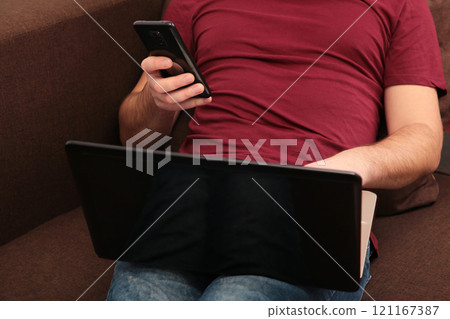 Young man working at home using laptop and smartphone Young man working at home using laptop and smartphone 121167387