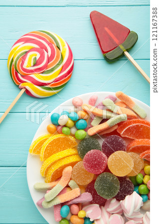 Colorful candies lollipops and jelly in plate on blue wooden background. Colorful candies lollipops and jelly in plate on blue wooden background. 121167388