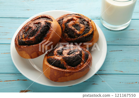 Bun with poppy seeds and glass of milk on blue wooden background. 121167550