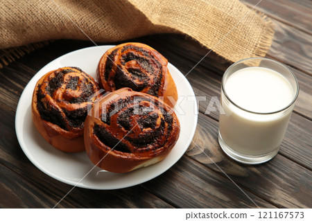 Bun with poppy seeds and glass of milk on brown wooden background. Bun with poppy seeds and glass of milk on brown wooden background. 121167573