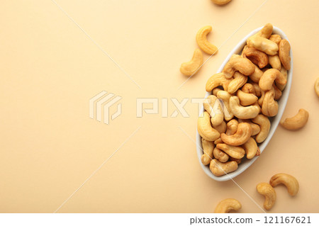 Cashew nuts on white plate on beige background. Top view. 121167621