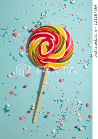 Colorful spiral lollipop with sprinkling on blue background. Vertical photo 121167664