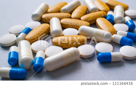 A collection of various pills, capsules, and supplements scattered on a gray surface. A collection of various pills, capsules, and supplements scattered on a gray surface. 121168438